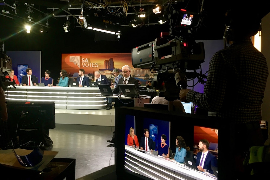 Wide shot of camera crews and production crew and election panel in TV studio.