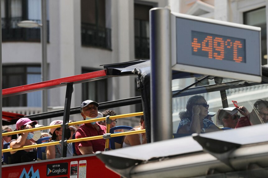 A tourist bus rides past a thermometer displaying 49 degrees Celsius.