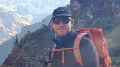 A man looks at the camera, surrounded by mountains