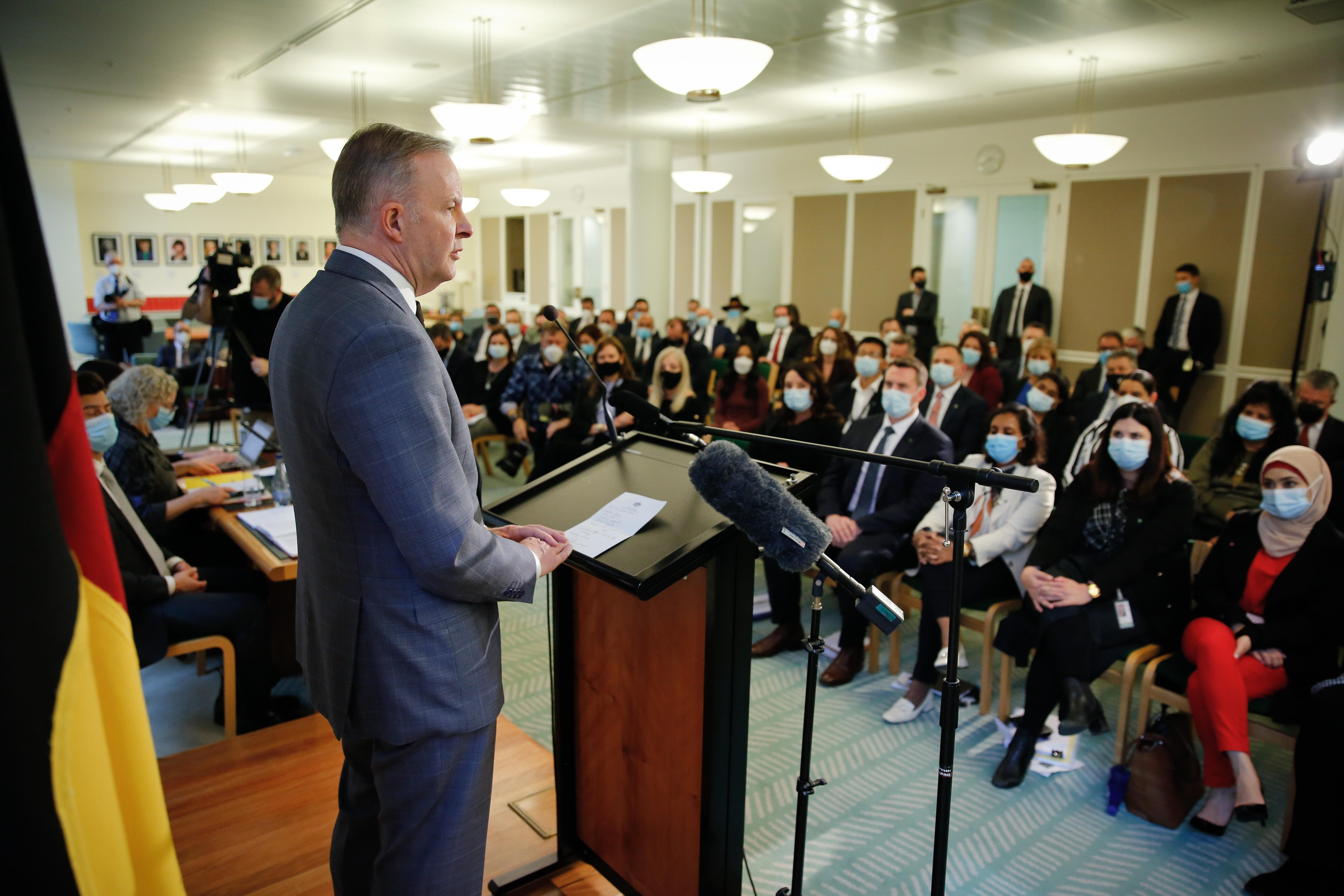 Albanese stands at a lectern looking out at rows of seated Labor politicians, inside their party room.