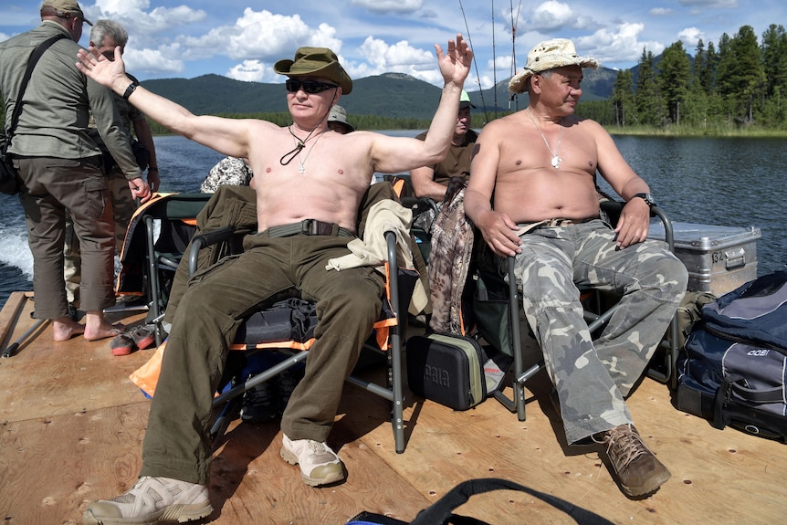 Vladimir Putin and Sergei Shoigu in matching cargo pants and hats on a boat. Both men are shirtless