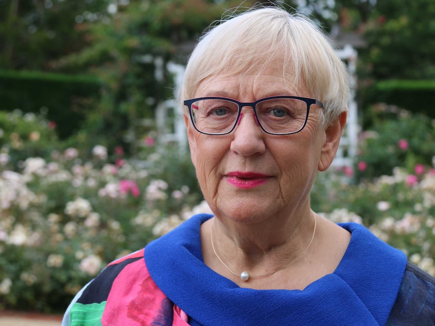 Robyn looks seriously into the camera, the flower garden in the background.