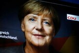 A billboard lit up at night features the face of Angela Merkel.