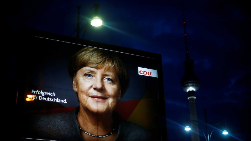 A billboard lit up at night features the face of Angela Merkel.