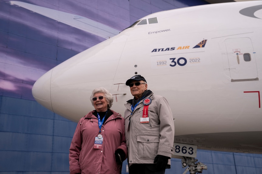 A couple stand in front of a jet plane.