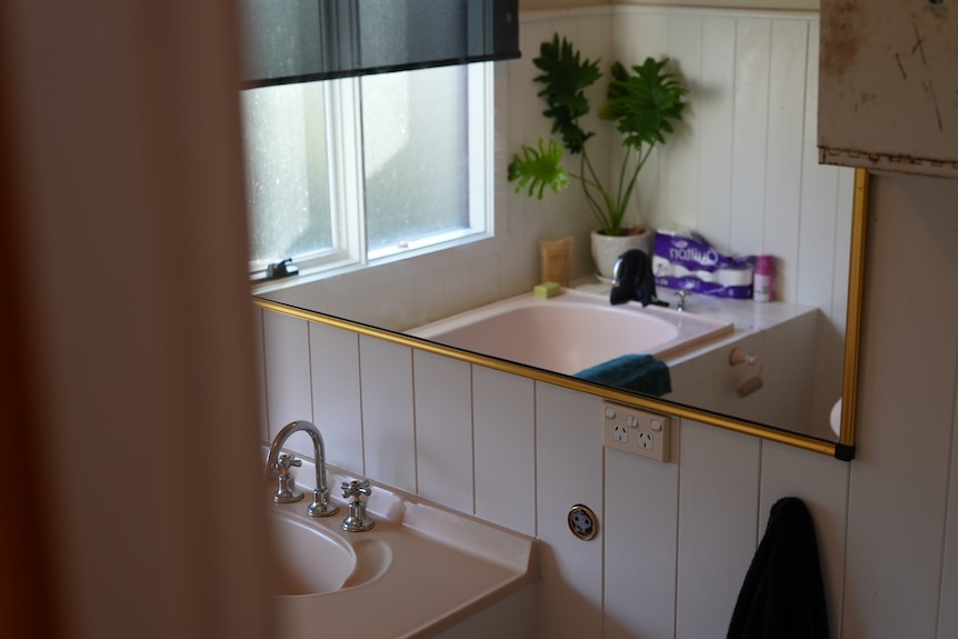 A bathroom sink and mirror with a window in the reflection.