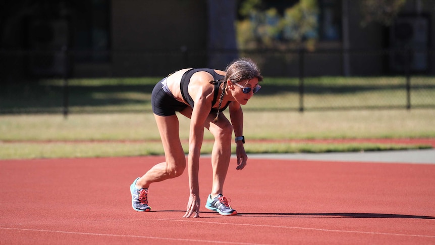 Runner in black shorts and top in a starting crouch on an athletic track.