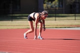 Runner in black shorts and top in a starting crouch on an athletic track.