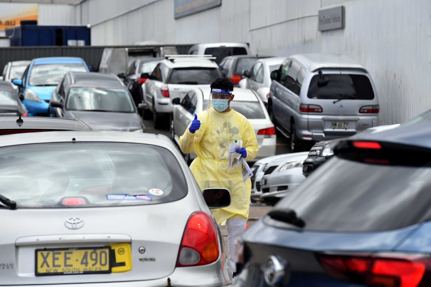 A health worker stands between cars at a covid testing station