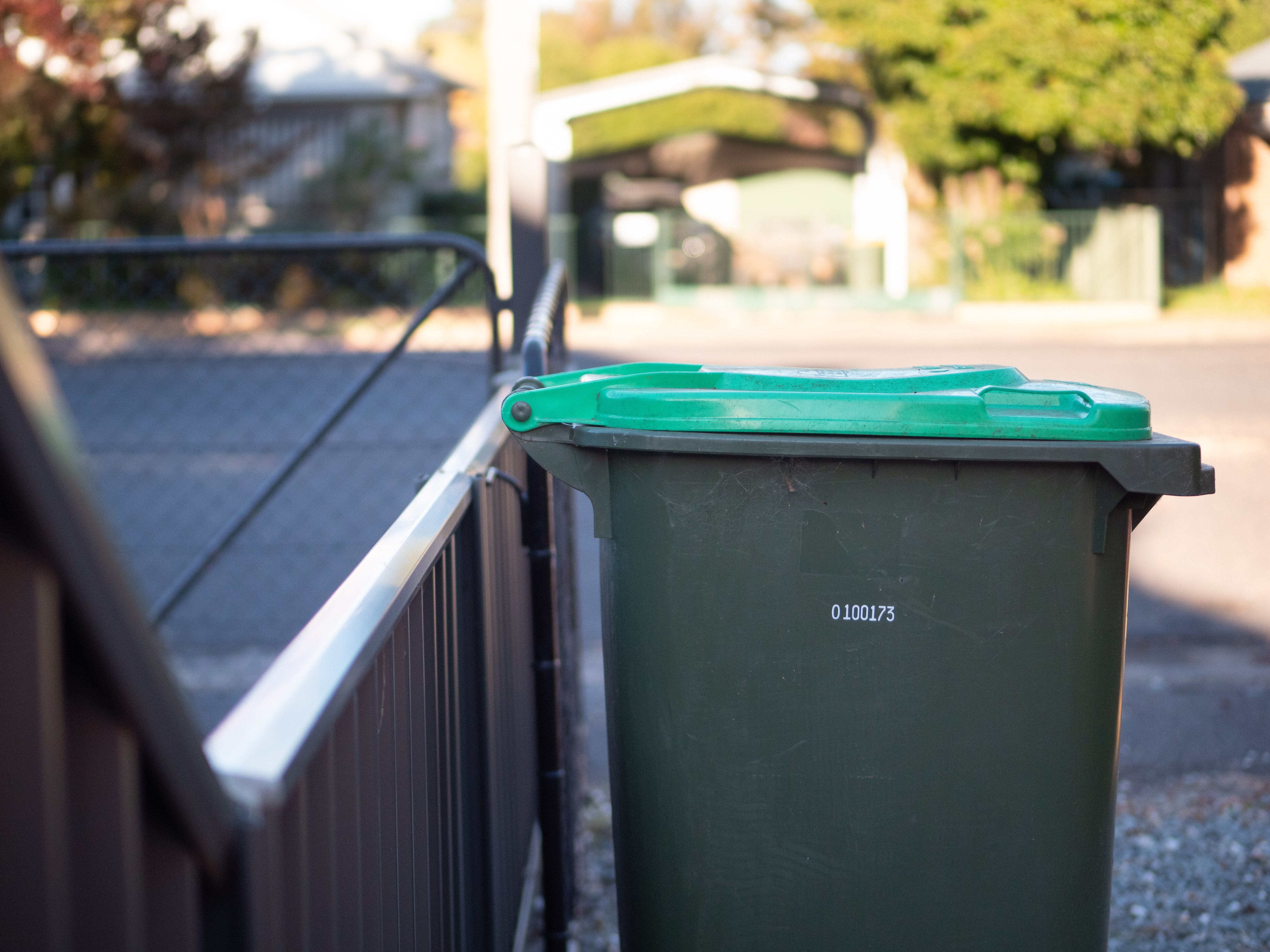 Contenedores comunitarios con tapas verdes en una calle suburbana.
