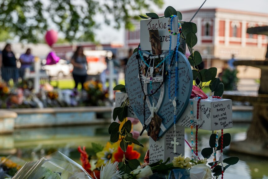 A white cross is covered with jewelry and flowers in memory of a shooting victim