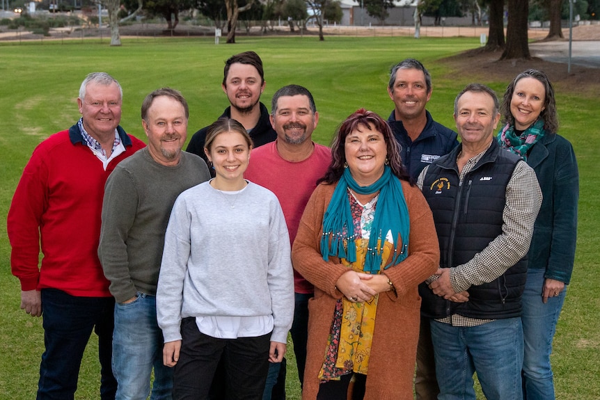 Nine people stand smiling on a green lawn.