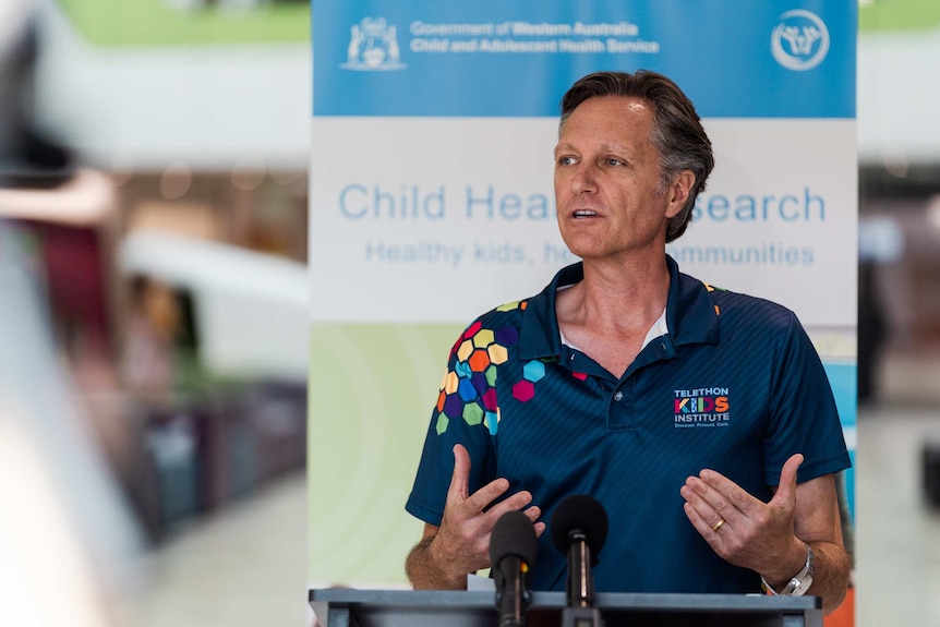 Man in telethon kids institute polo shirt speaks behind podium