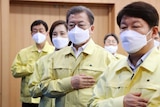 A group of people wearing masks and yellow raincoats raise their right hands to their chest.