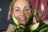 A woman with blonde hair and blue eyes holding up flowers