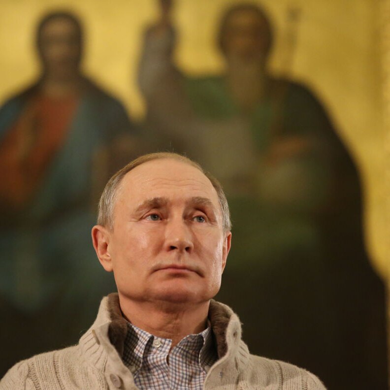 Close up of Russian President Vladimir Putin standing in front of a blurred painting of Jesus and a prophet on gold background