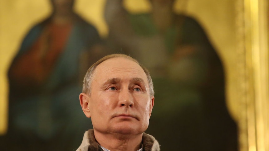 Close up of Russian President Vladimir Putin standing in front of a blurred painting of Jesus and a prophet on gold background