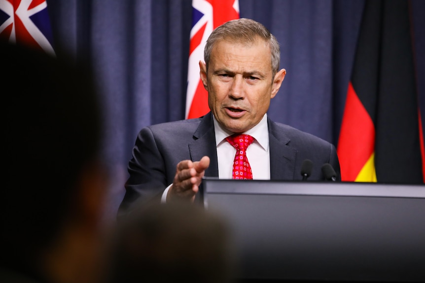 Roger Cook pointing while standing at a lectern.