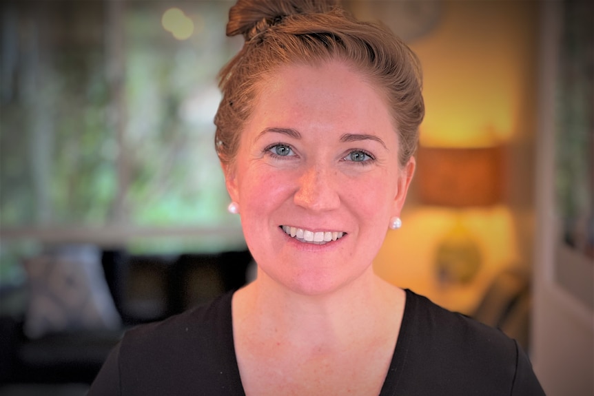 A woman with red hair and blue eyes smiles for the camera. 