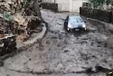 A grey Prius is washed down a street by a mudslide.