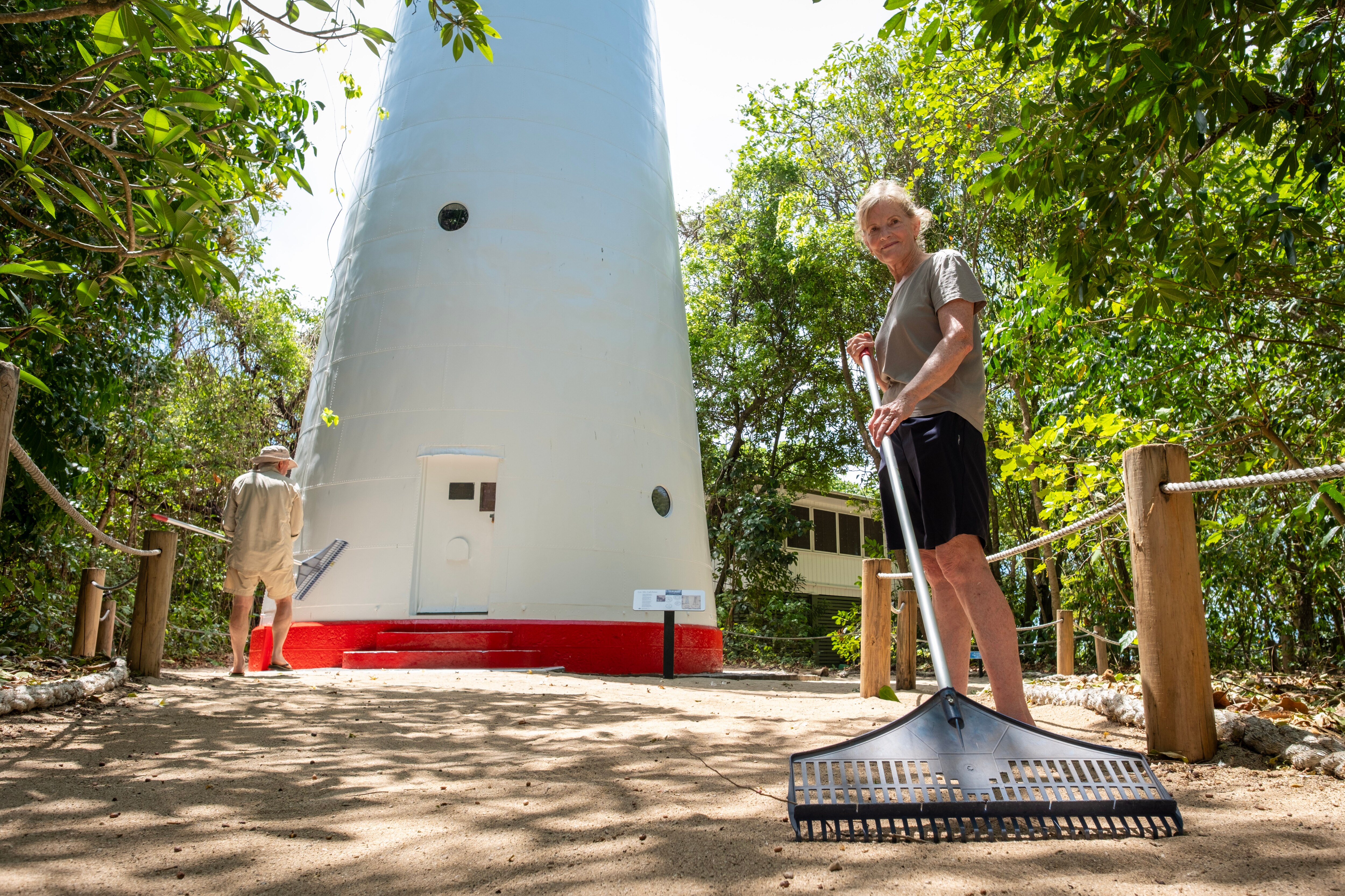 Woman raking in front of white and red lighthouse