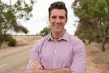 SA Liberal MP Fraser Ellis standing in front of country road with his arms crossed smiling.