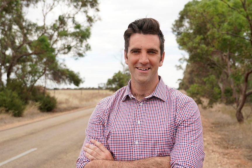 SA Liberal MP Fraser Ellis standing in front of country road with his arms crossed smiling.