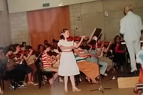 A young girl in a white dress plays violin in a hall