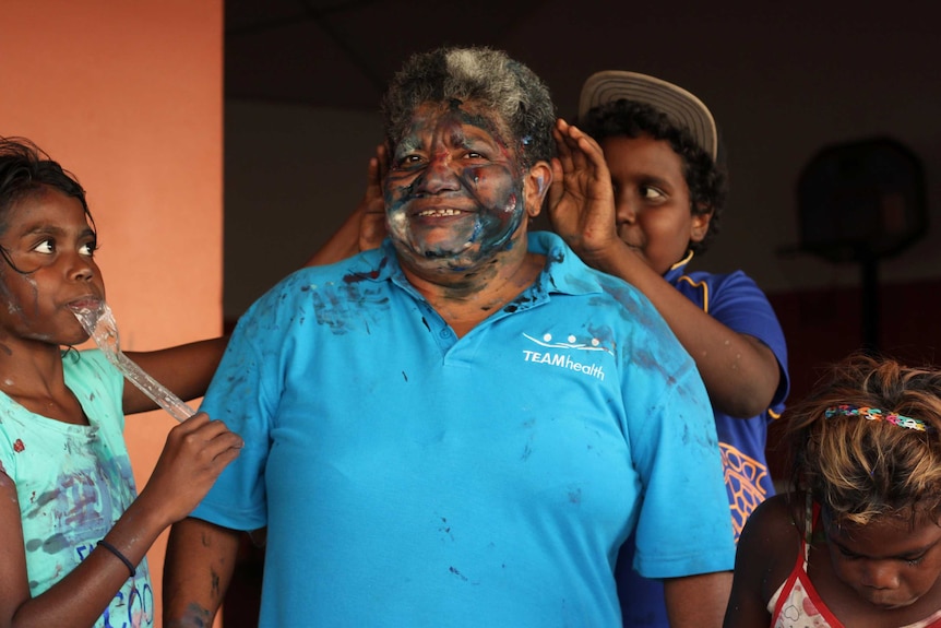 A woman covered in painted with children around her.