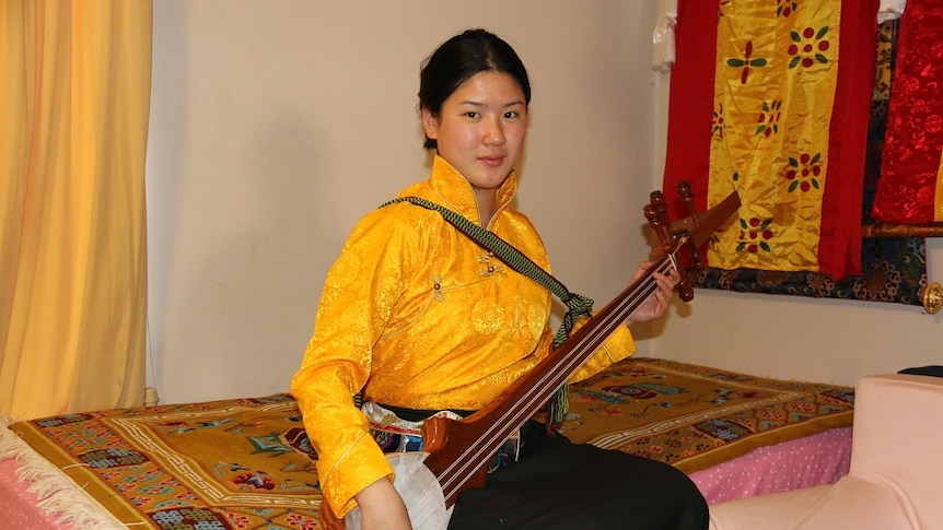 Young woman in cultural dress holds a Sangen, a three stringed traditional guitar, in her room