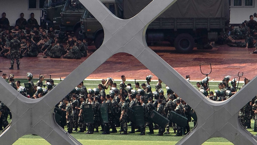 Looking from behind a fence, the shot is of Chinese military troops practicing drills in a Shenzhen stadium