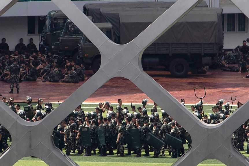 Looking from behind a fence, the shot is of Chinese military troops practicing drills in a Shenzhen stadium