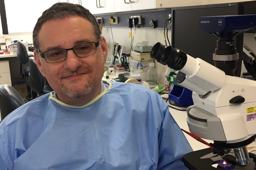 doctor in scrubs in front of microscope