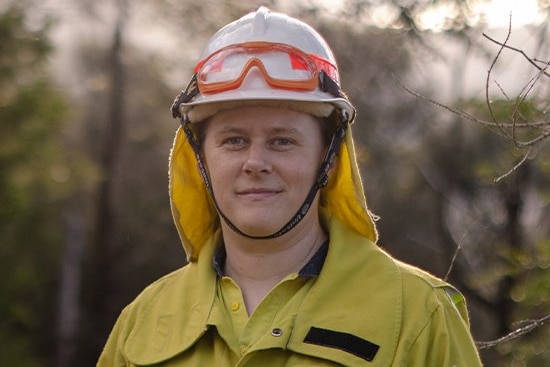 Woman in fire gear, wearing helmet with goggles sitting above helmet visor.