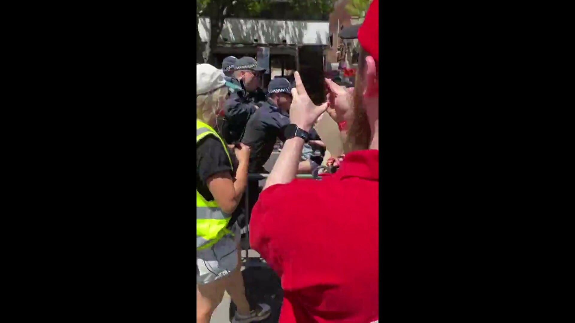 Police clash with a protester while a man films on his phone.