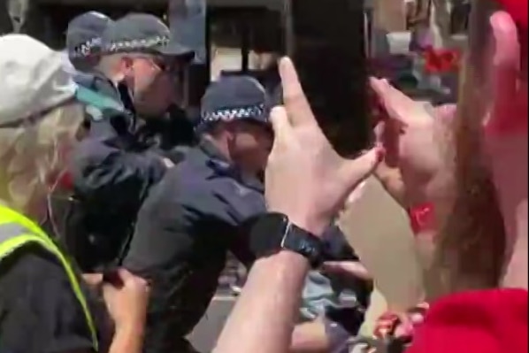 Police clash with a protester while a man films on his phone.