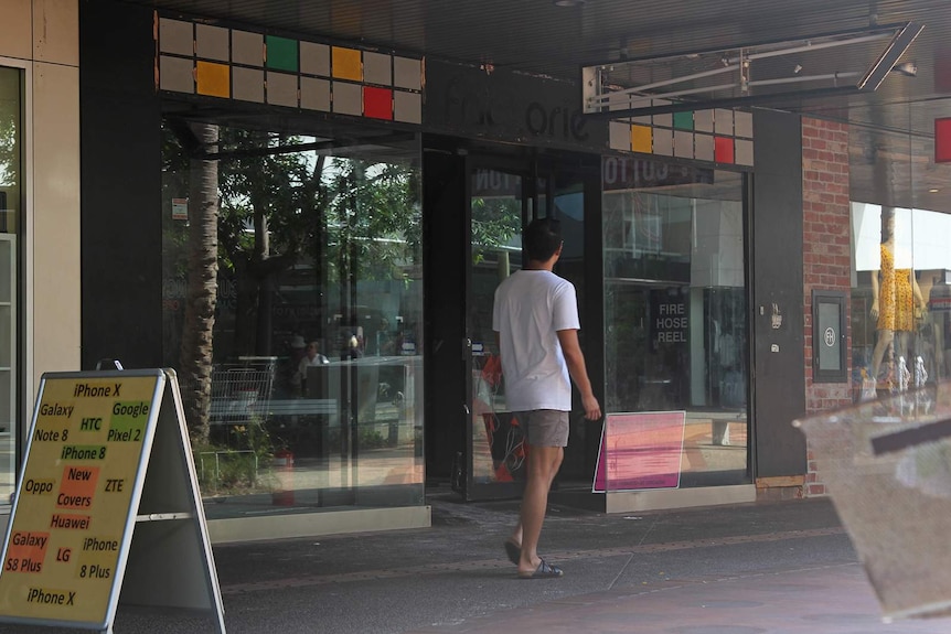 A man walking in front of an empty Darwin shopfront.
