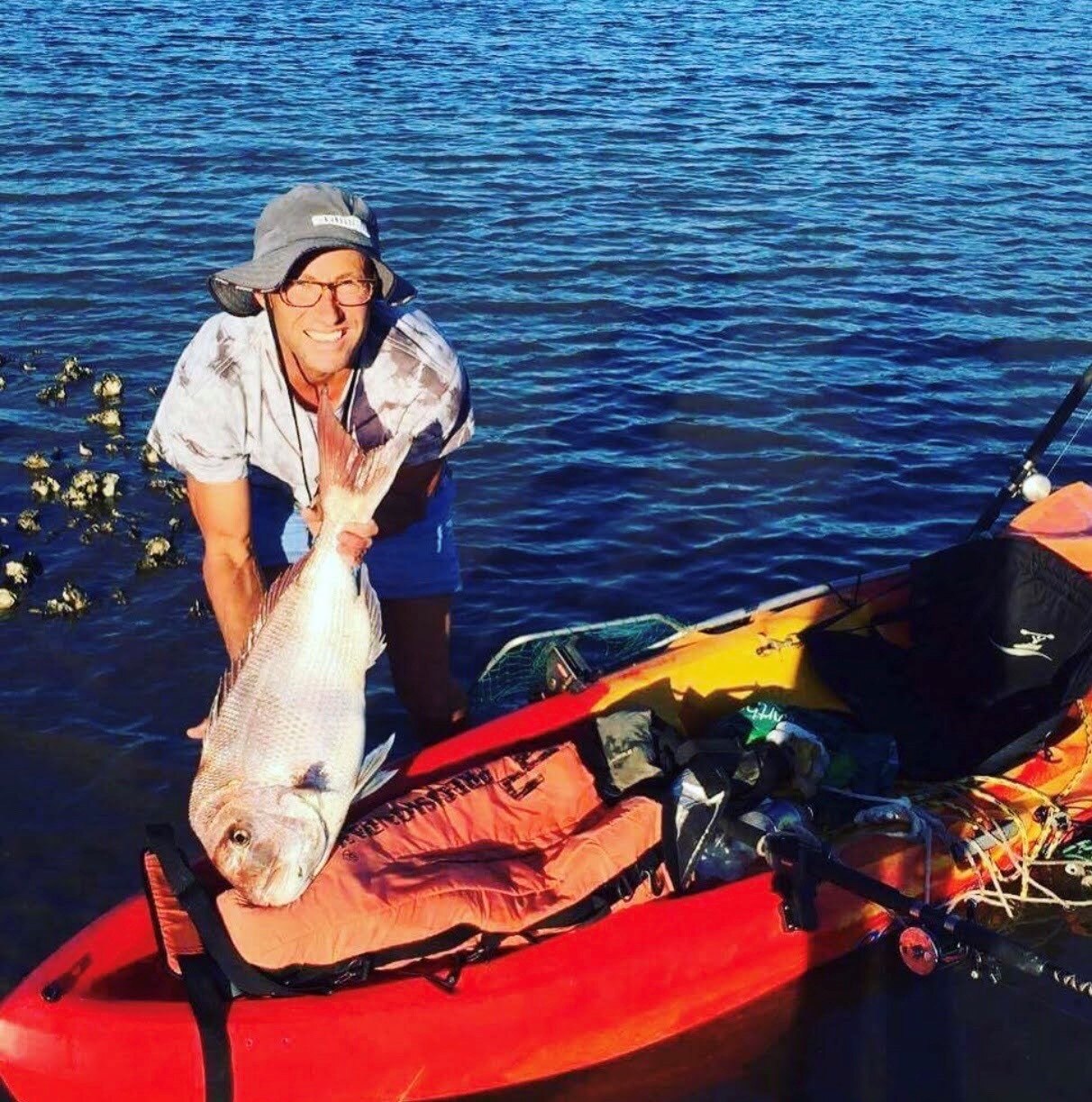 man holding a big fish, standing next to kayak