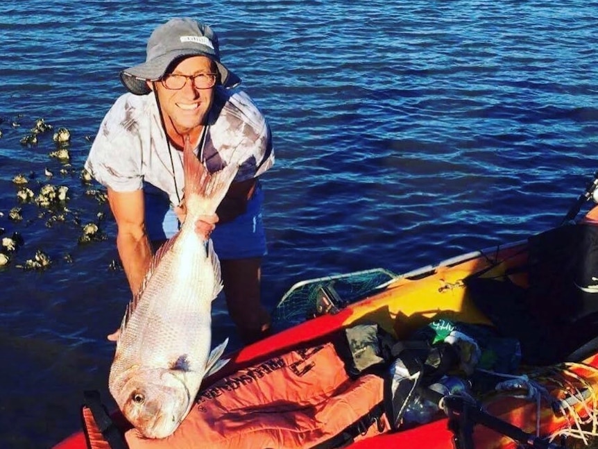 man holding a big fish, standing next to kayak
