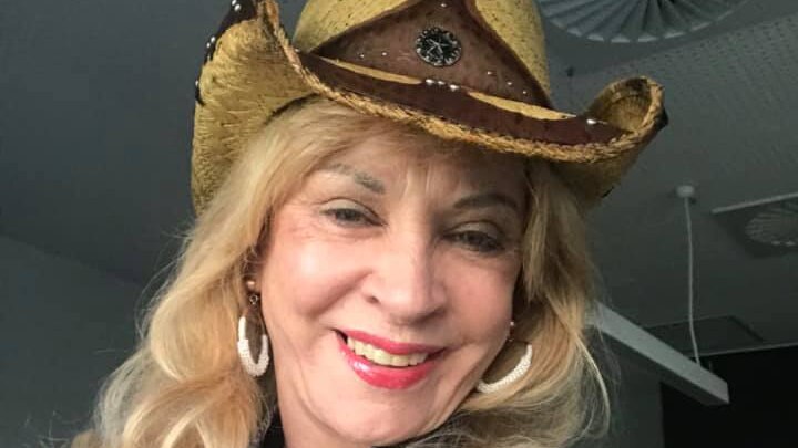 a woman with long blonde hair wearing  cow boy hat smiling at the camera