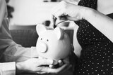 A woman deposits a coin into a piggy bank being held by a man.