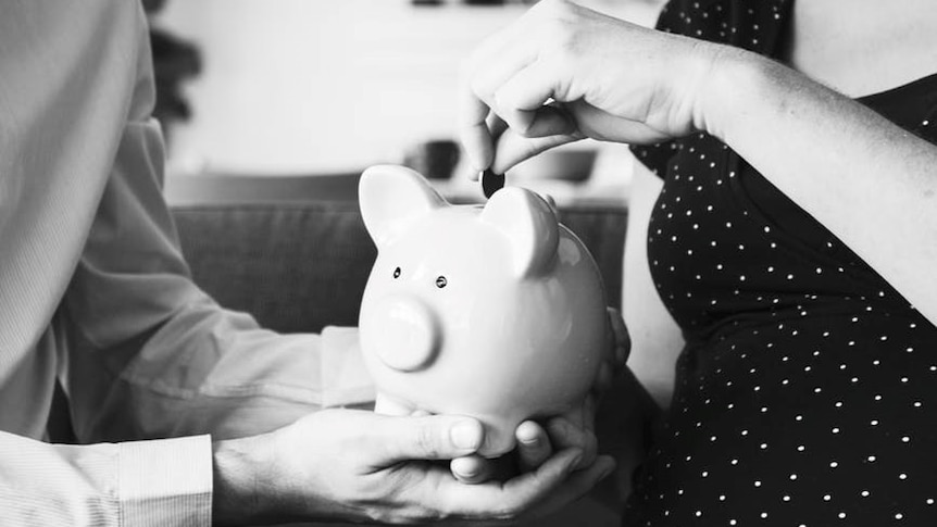 A woman deposits a coin into a piggy bank being held by a man.