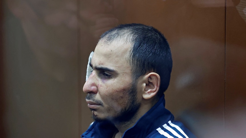 A man is pictured from the left side profile, his face bruised. On the right side of his head a bandage.