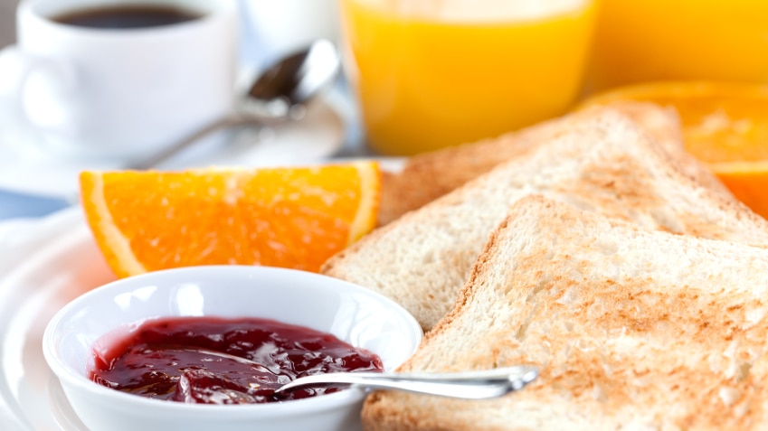 A piece of toast with a small bowl of jam, a slice of orange and a glass of orange juice.