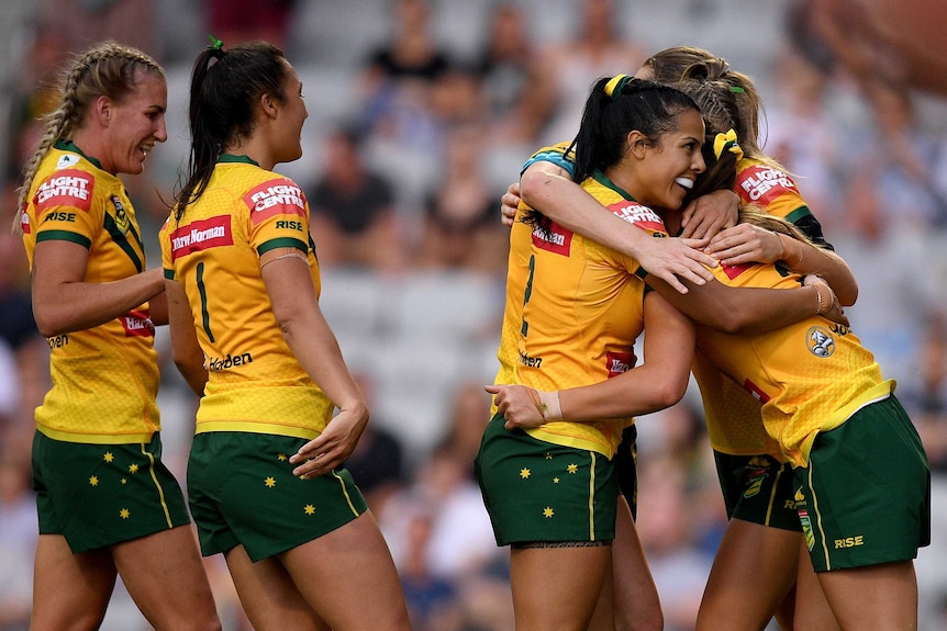 Jillaroos players embrace each other as they celebrate a try against the Kiwi Ferns.