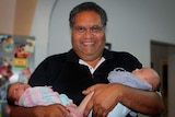Man who is Indigenous with twin babies, one cradled in each arm.