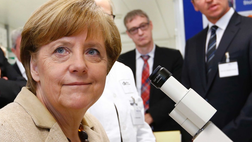 Angela Merkel smiling while sitting in front of a microscope