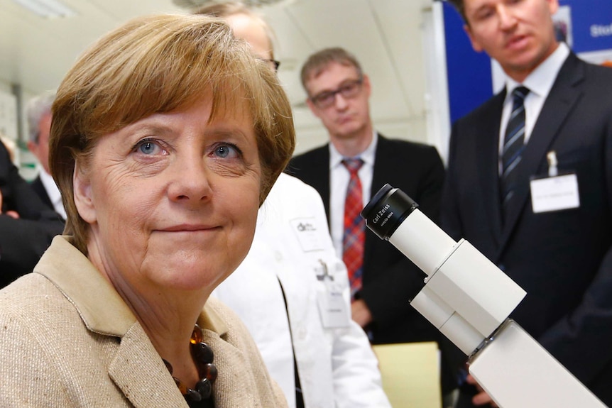 Smiling Angela Merkel sitting in front of a microscope