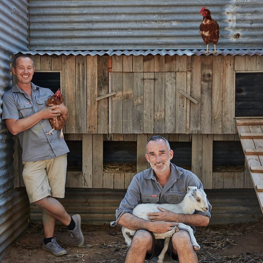 One man is holding a chicken and another man is holding a goat.