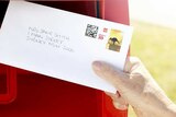 A woman places a letter in an Australia Post box.